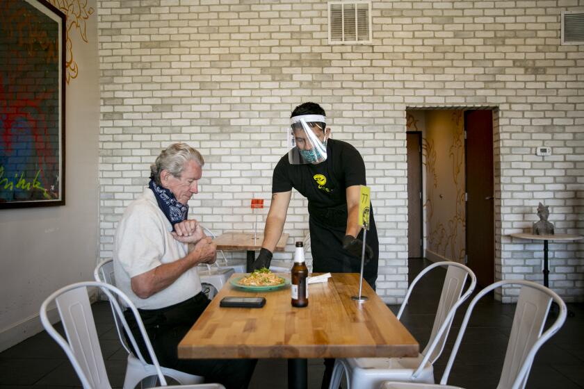 Shift leader Jonathan Garcia delivers a meal to Darryl Thibault of Bay Ho as diners eat at Saffron Thai on May 21, 2020 in San Diego, California. Restaurants began reopening for dine-in patrons on Thursday as the state and county began easing restrictions imposed during the coronavirus pandemic.