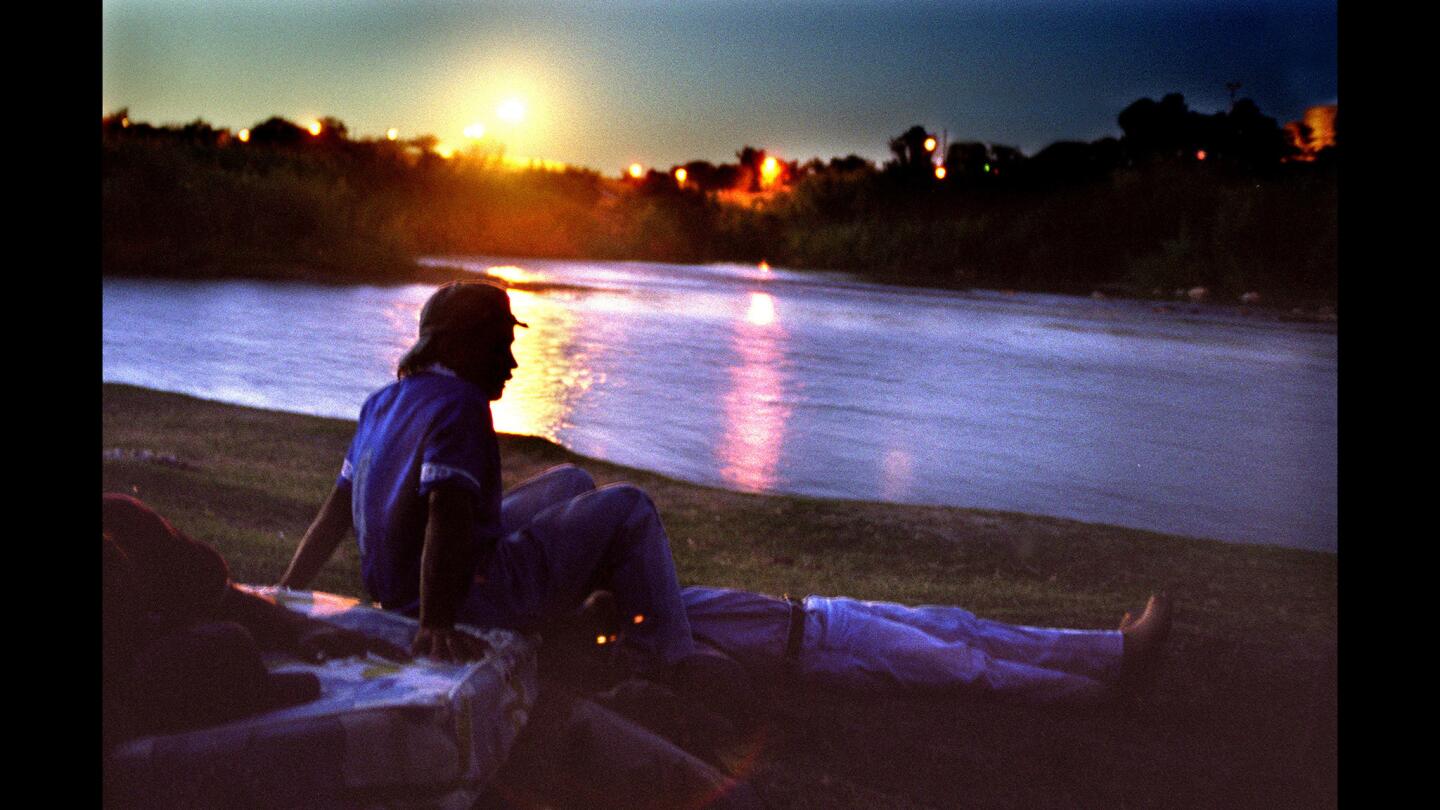 Young Honduran migrants rest on the Mexican side of the Rio Grande. In the distance, U.S. Border Patrol lights illuminate Zacate Creek in Texas.