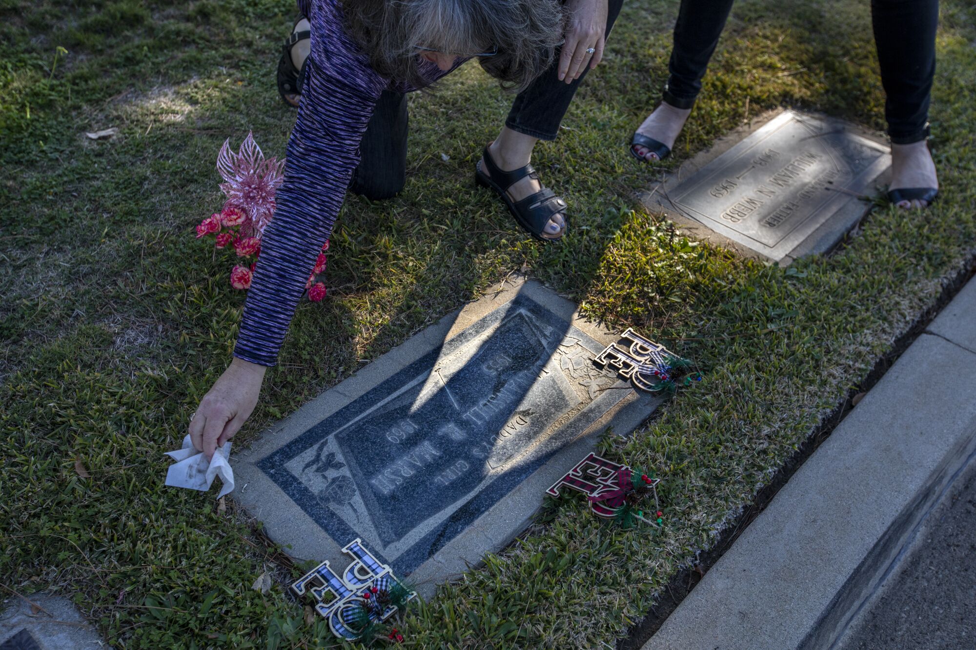 A woman uses a white cloth to dust off a grave that reads "Janansull R. Marsh, 1955 to 1969"