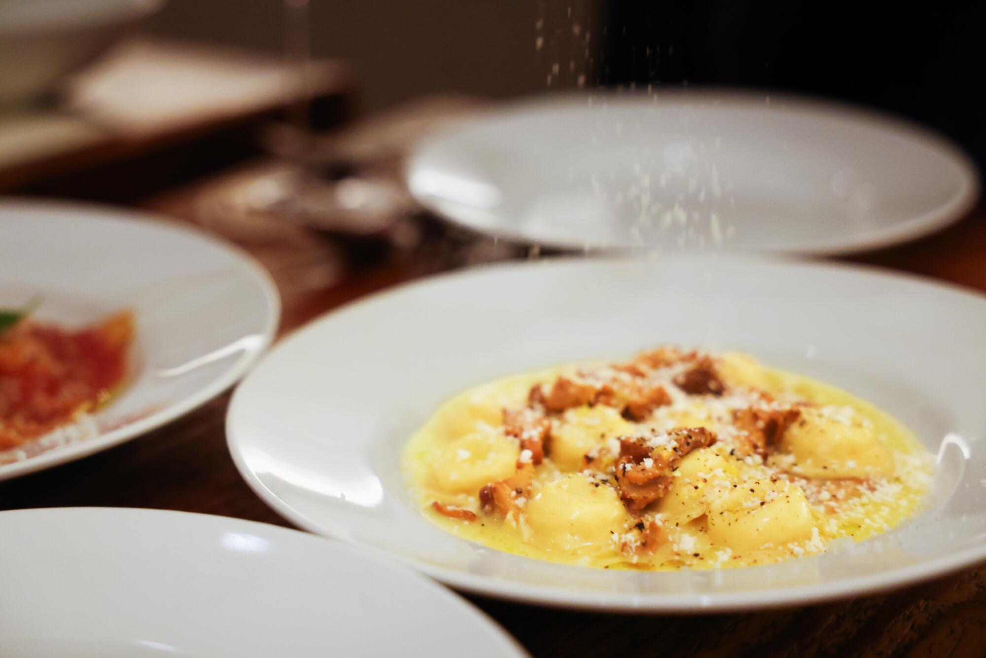 A plate of pasta being dusted with parmesan.