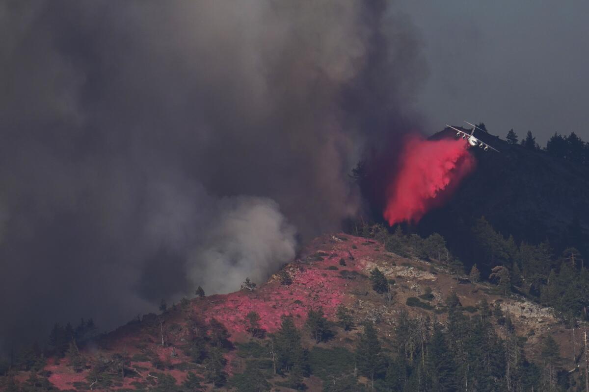 Pink fire retardant stains a ridgetop and falls from a jet flying over black smoke 