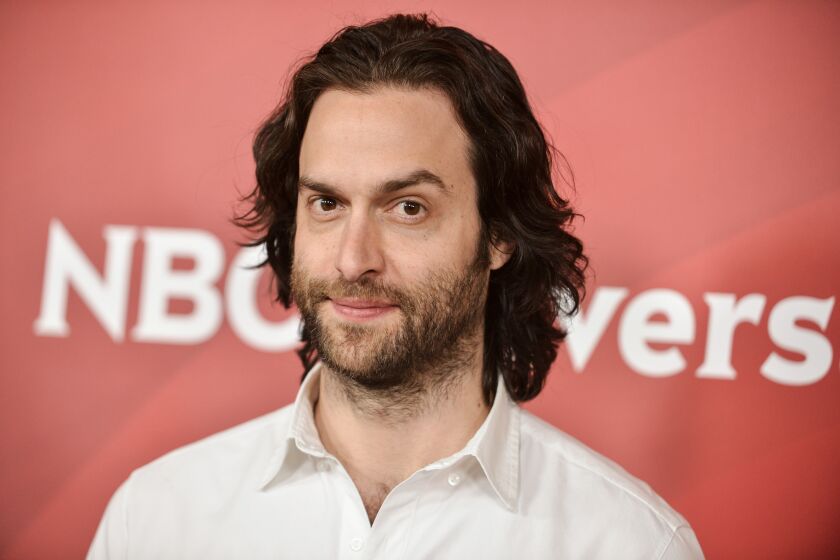 Chris D'Elia poses in a white collared shirt while looking directly into the camera.