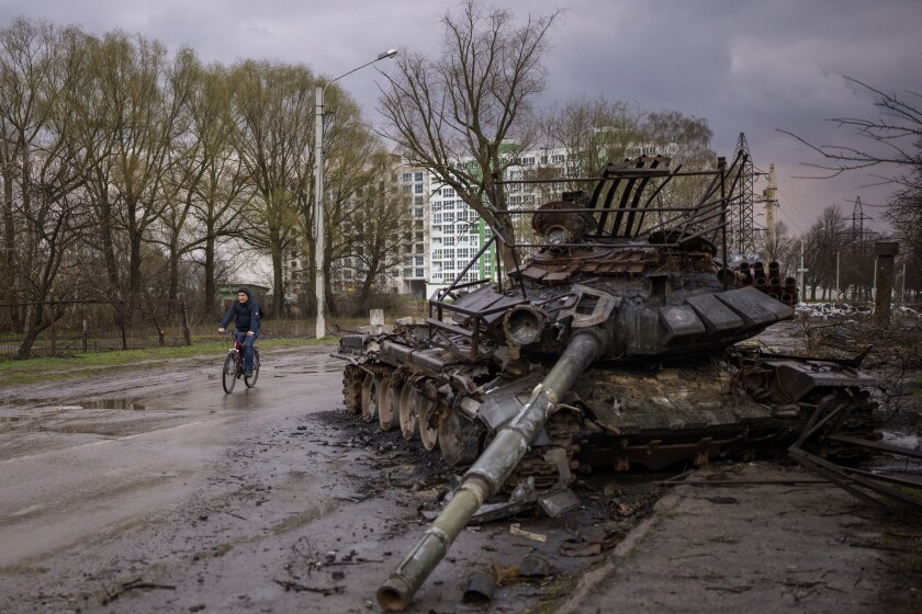 A man rides his bicycle next to a destroyed Russian tank in Chernihiv, Ukraine