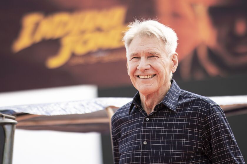 Harrison Ford in a dark flannel shirt poses in front of an Indiana Jones banner at Cannes