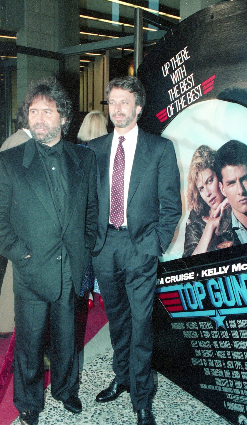 Producers Don Simpson and Jerry Bruckheimer stand in front of Top Gun movie poster 
