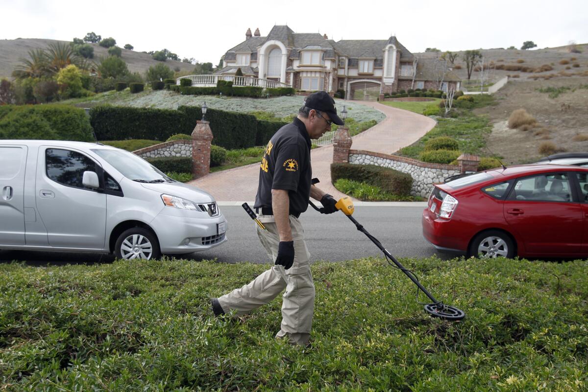 An Orange County Sheriff's Department member searches for a weapon and evidence in February near the mansion where a San Juan Capistrano couple were killed.