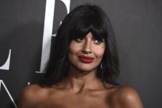 Jameela Jamil poses in red lipstick and a sleeveless dress.
