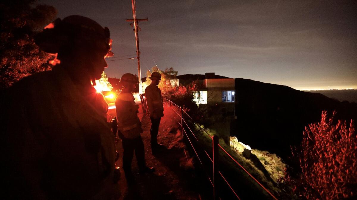 Los Angeles County firefighters look over a landslide at the base of a home along Hume Road in Malibu.
