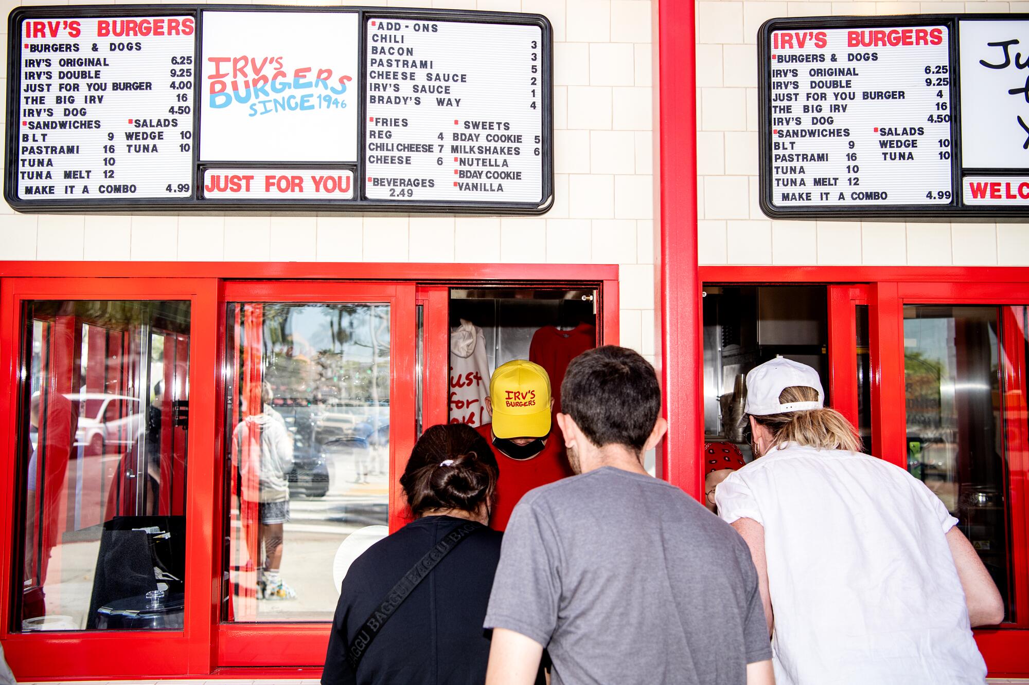 A trio of customers stands at the Irv's Burgers order window, their backs to the camera.