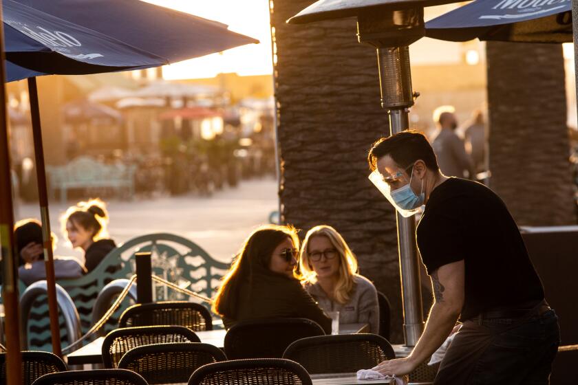 HERMOSA BEACH, CA - NOVEMBER 25: A server at Rebel Republic cleans tables on Pier Plaza in Hermosa Beach, CA, on the final afternoon before a 10 p.m. end to outdoor dining because of the increase in COVID-19 cases, Wednesday, Nov. 25, 2020. (Jay L. Clendenin / Los Angeles Times)