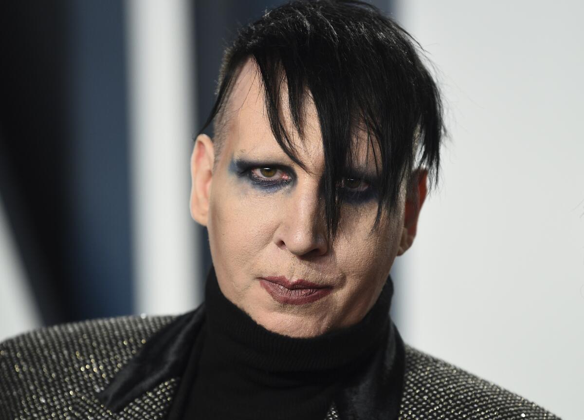 Marilyn Manson wears smeared makeup and a sparkly, turtleneck outfit.