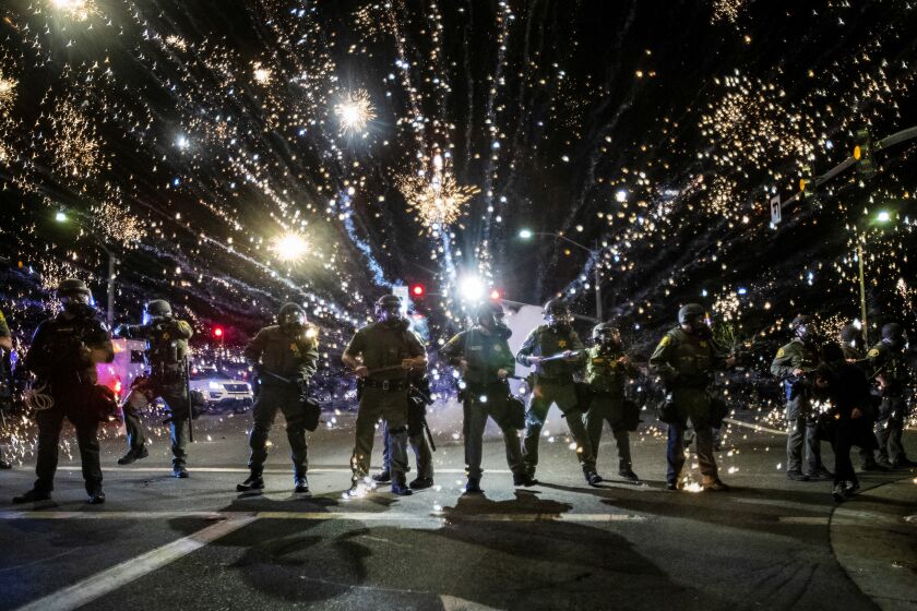 SANTA ANA, CA - MAY 30, 2020: Orange County Sheriff deputies maintain a police block as a firecracker thrown by a protester explodes behind them during a protest against the Minneapolis police killing of George Floyd during the coronavirus pandemic on May 30, 2020 in Santa Ana, California.