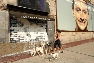 HOLLYWOOD, CA. JULY 15, 2021 - Dog walker Samantha Ahrem walks past mural of George Floyd on Laugh Factory that was defaced in last several days on Thursday, July 15, 2021. (Al Seib / Los Angeles Times)