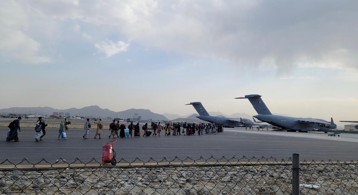 A line of evacuees on an airport tarmac near aircraft.