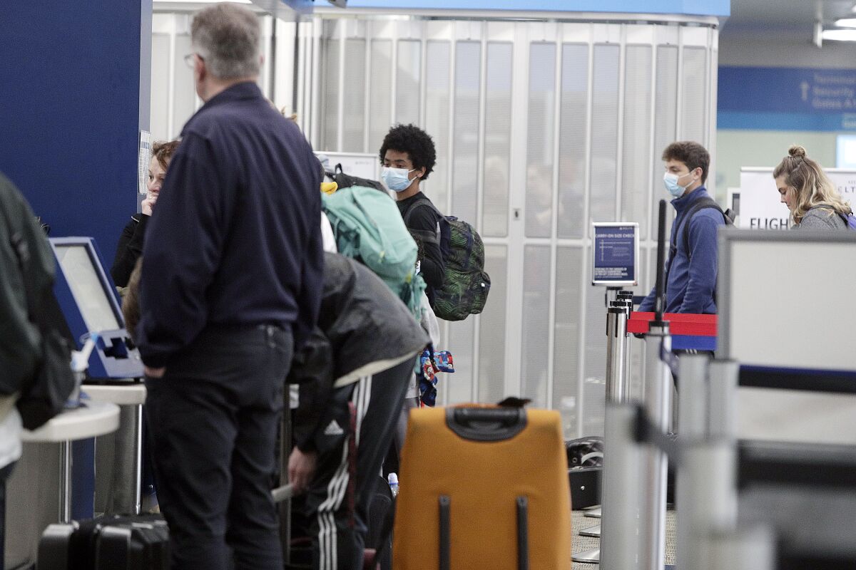 Passengers wearing facemasks wait in line at the check-in counter at Terminal B at the Hollywood Burbank Airport on Tuesday, March 17.