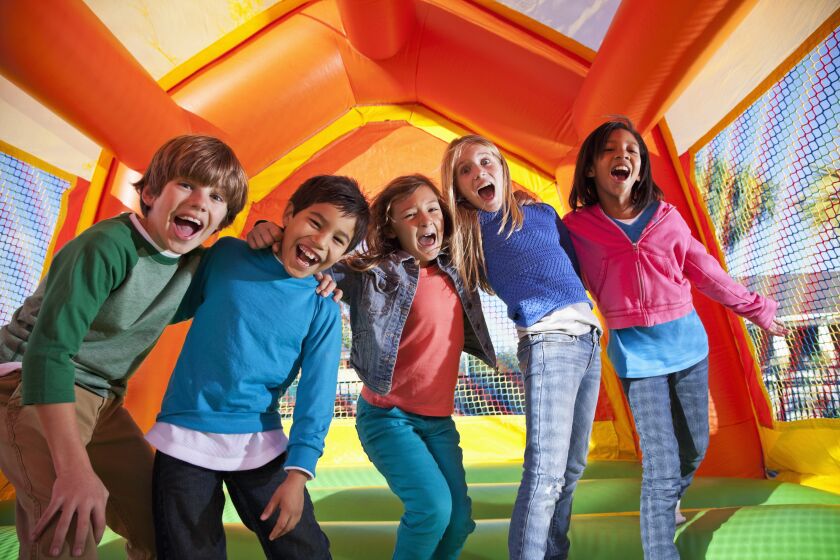 A group of five young children laughing in an orange, yellow and green bounce house. 