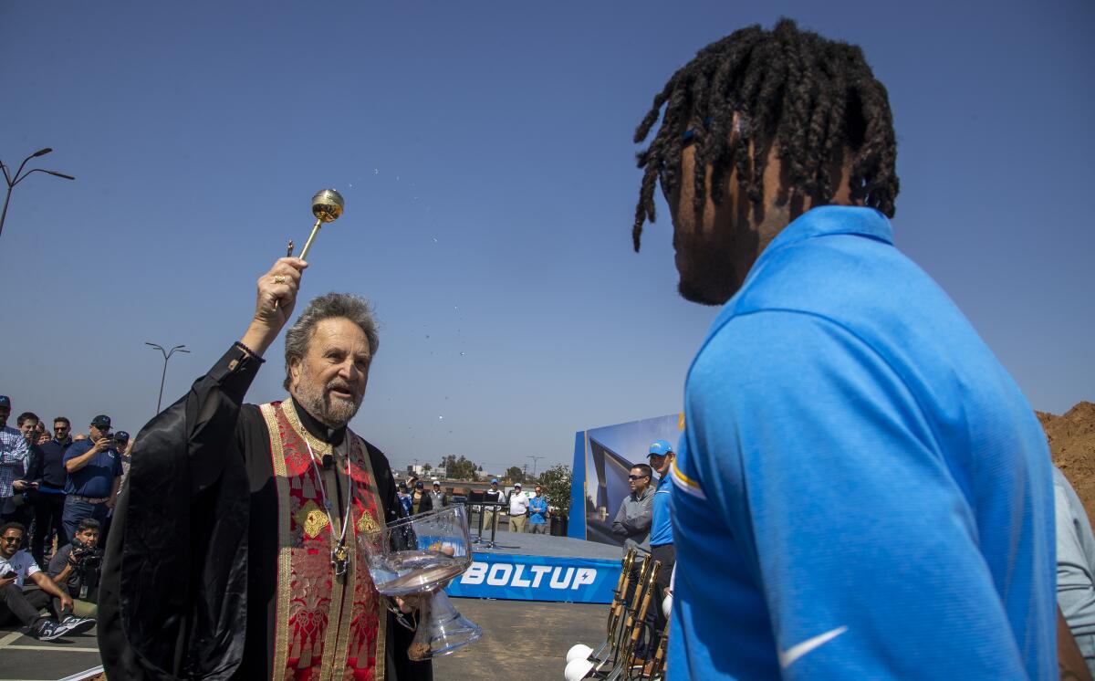 Father John Bakas splashes holy water on Chargers safety Derwin James during the L.A. Chargers groundbreaking ceremony.