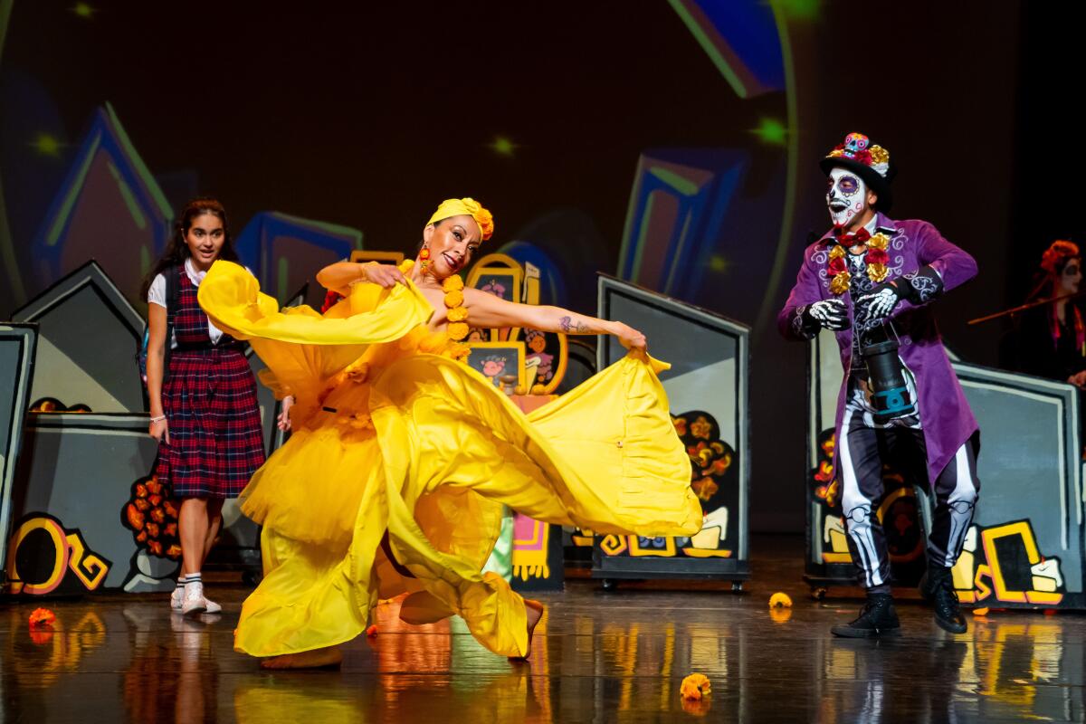A woman in a yellow dress dances onstage with a schoolgirl and a skeleton figure. 