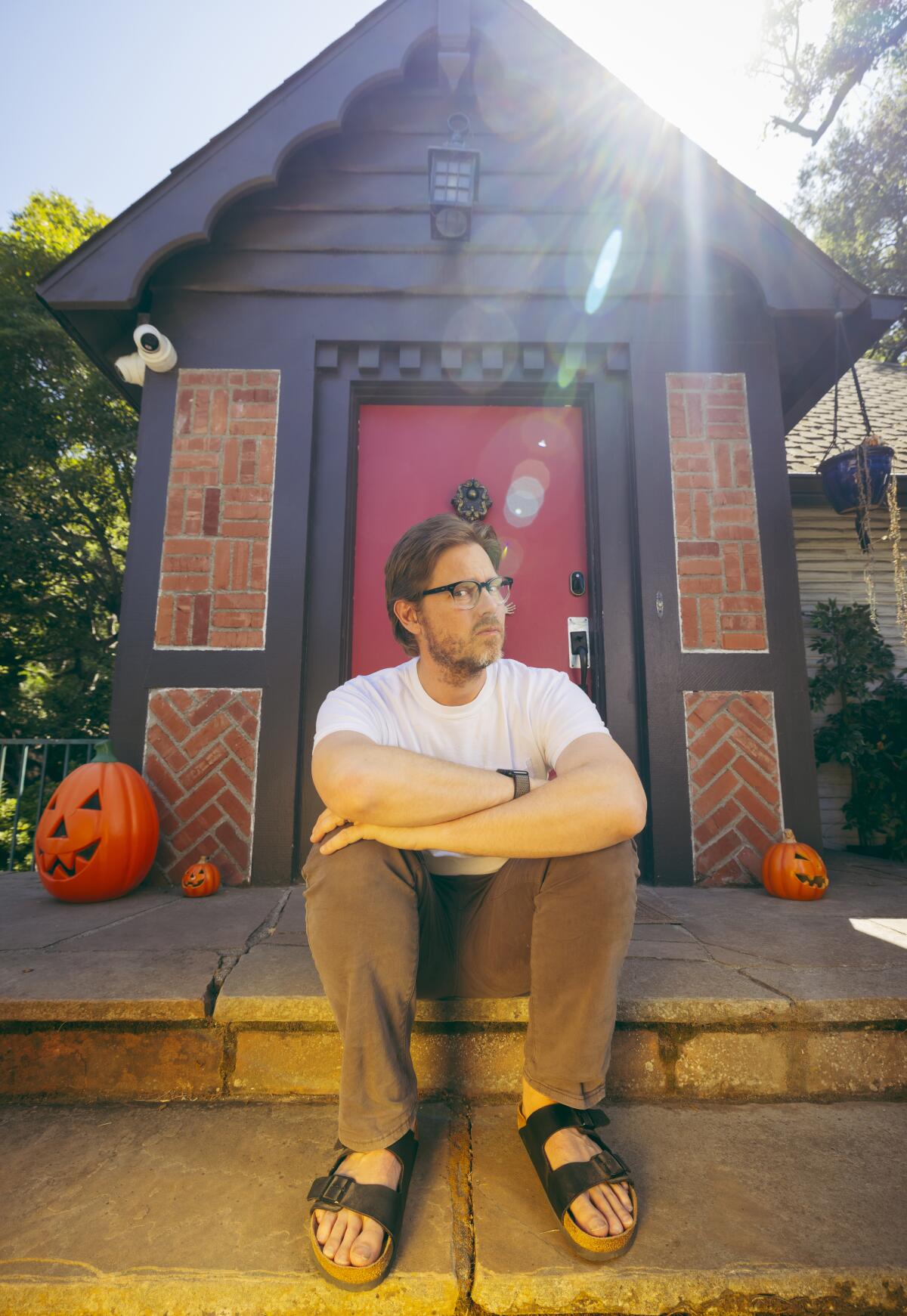 Man wearing sandals sitting in front of a shed 