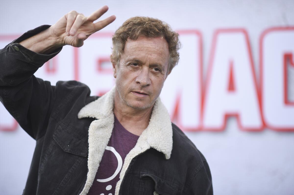 Pauly Shore making a peace sign in front of a white backdrop