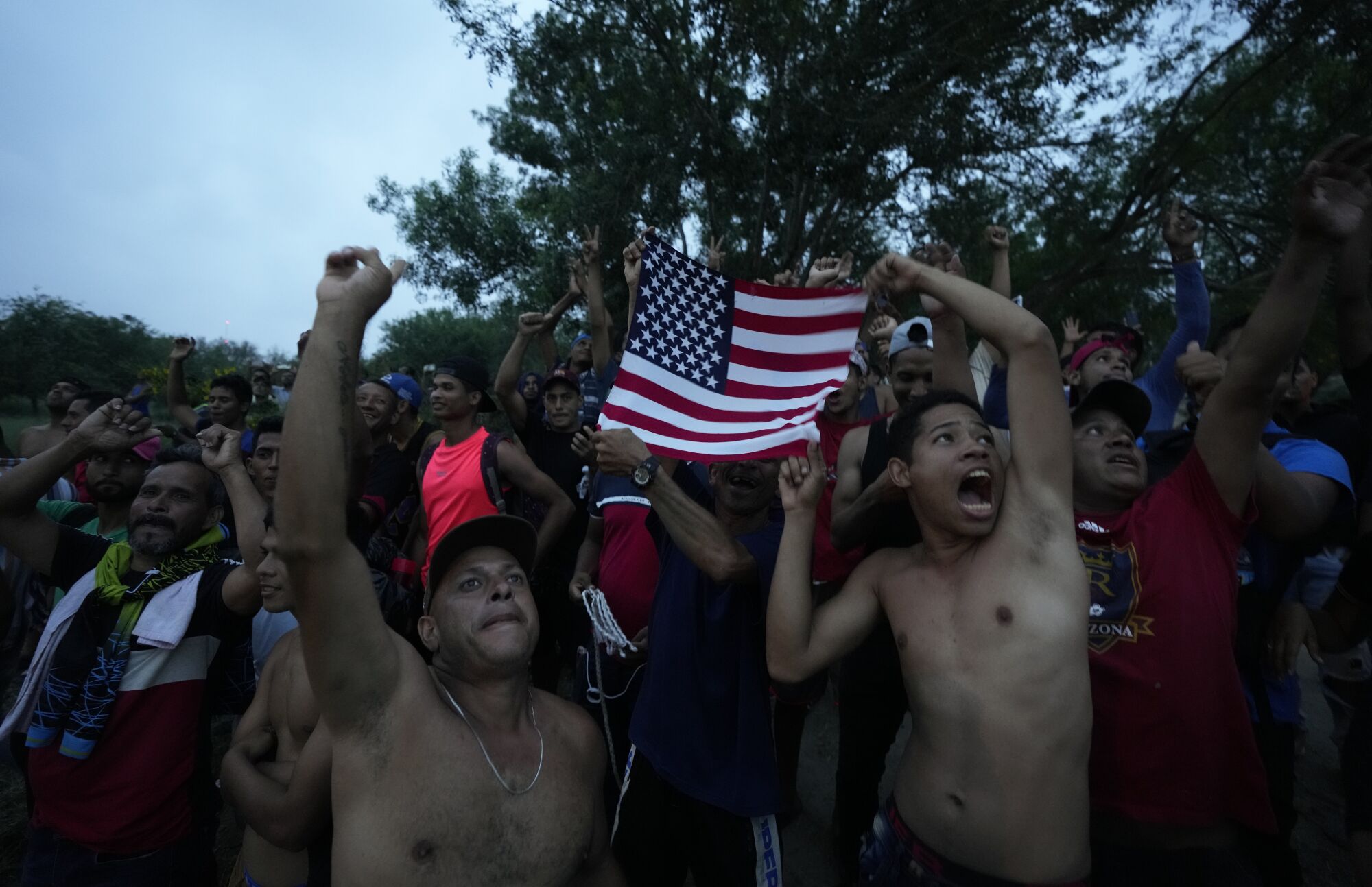 Venezuelan migrants wave a U.S. flag at a television helicopter that flew over the Rio Grande