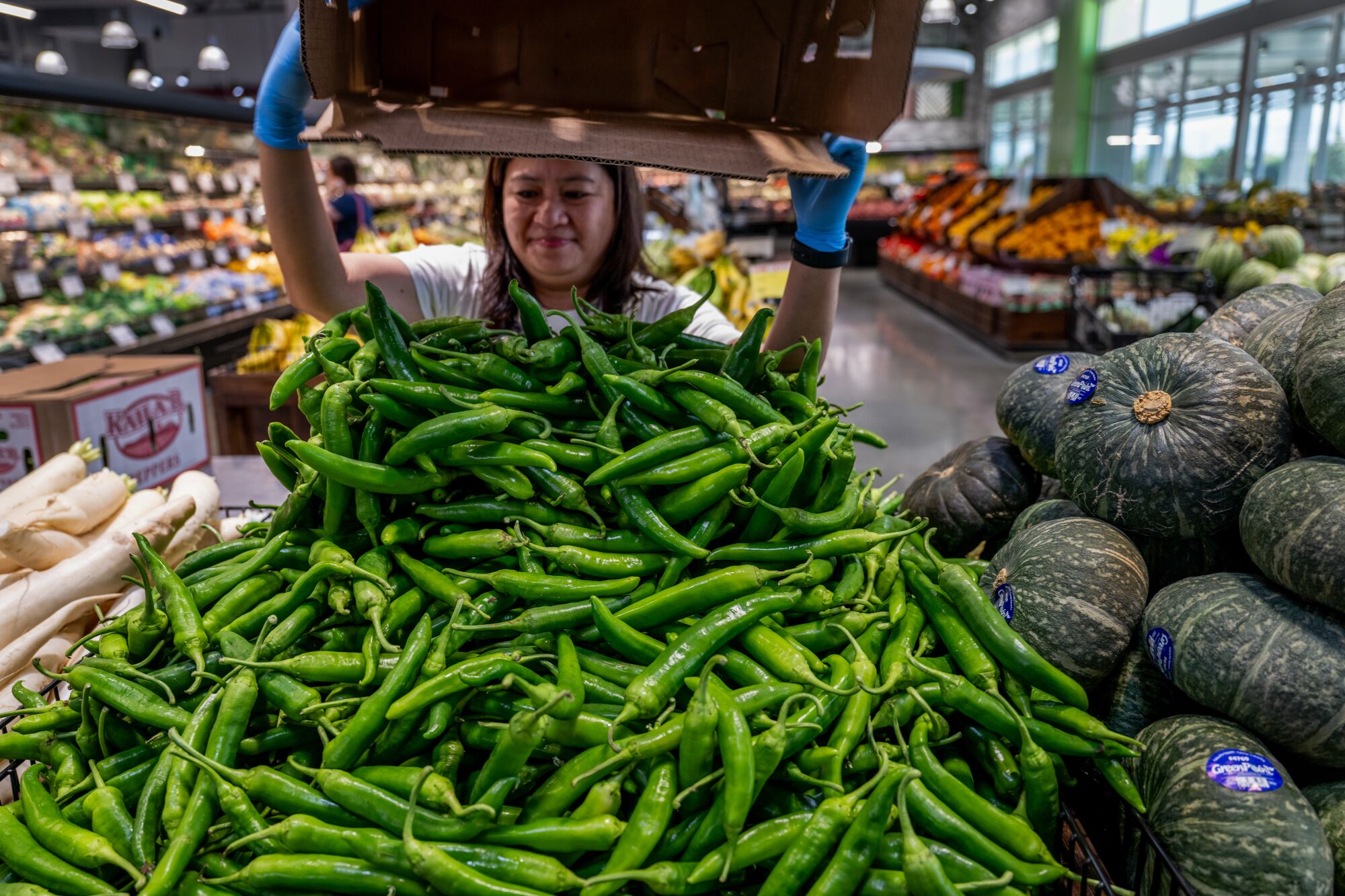 Un commis de magasin ajoute plus de piments doux frais à une pile d'affichage dans la zone des produits.