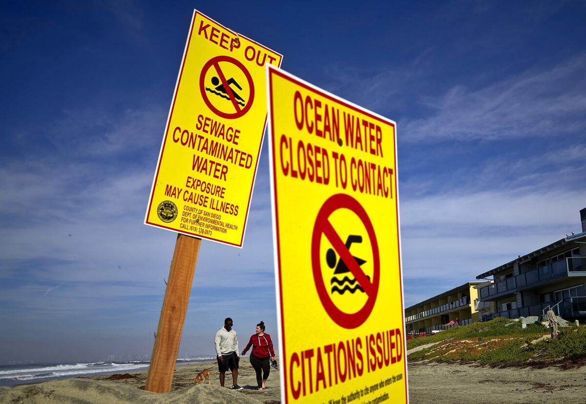 A couple walks along Imperial Beach, Calif., on Wednesday as signs warn of contaminated water.