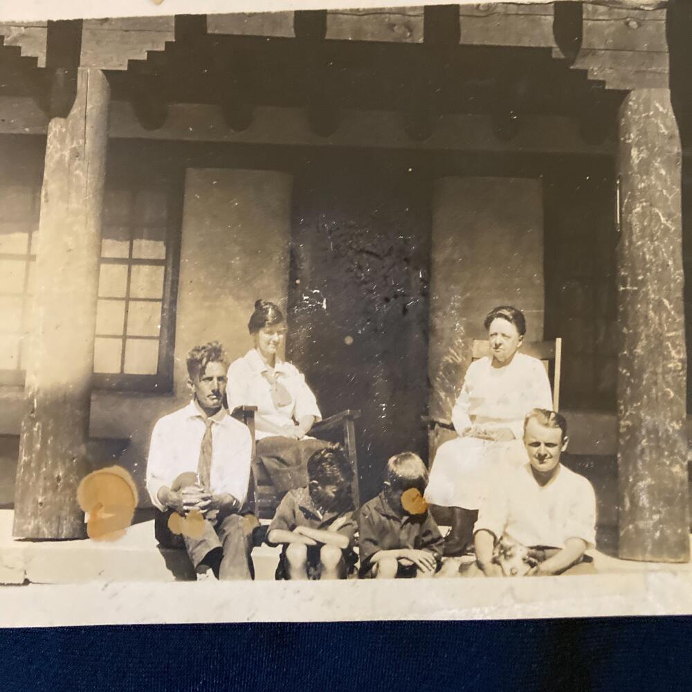 An old photograph from circa 1930 of four adults and two children sitting on a stoop