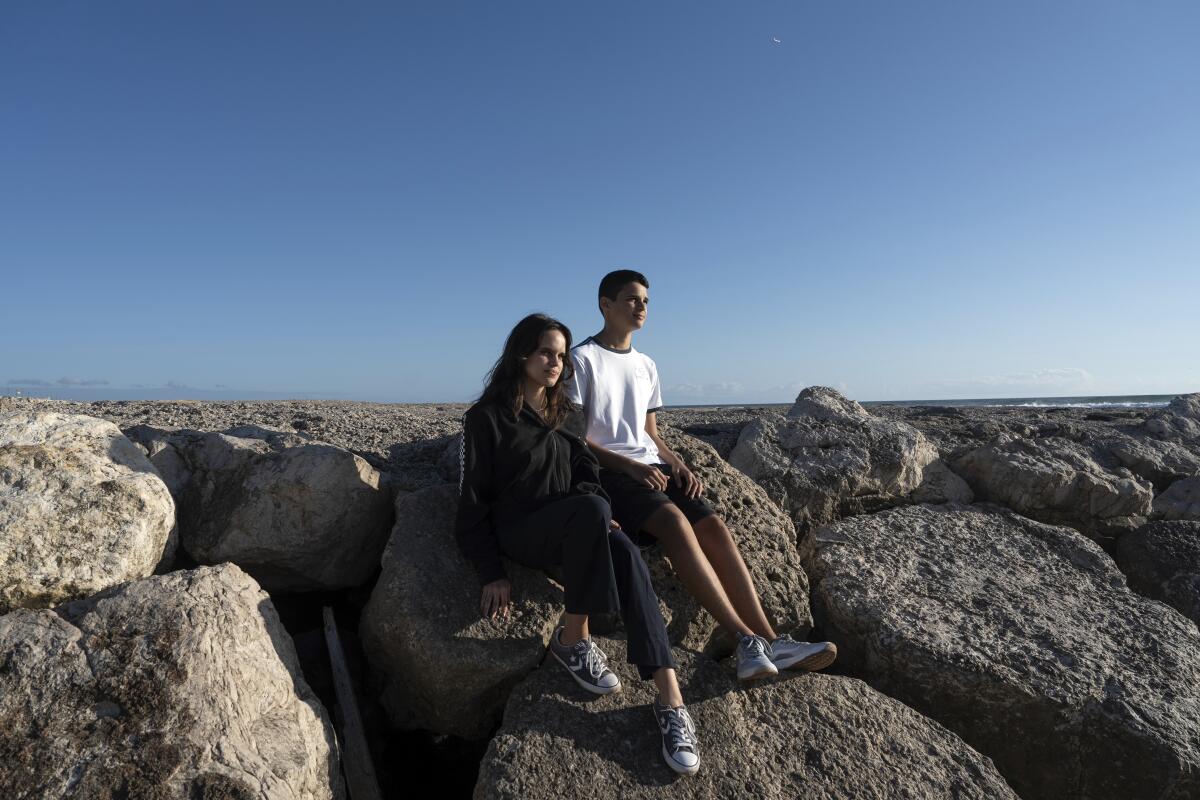 Siblings Sofia Oliveira, 18, and Andre Oliveira, 15, pose for a picture on boulders at a beach in Portugal.