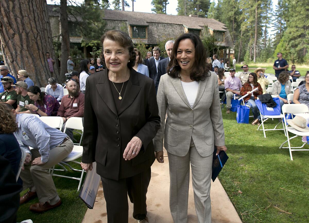 Sen. Dianne Feinstein and Vice President Kamala Harris  walk together near people sitting outdoors.
