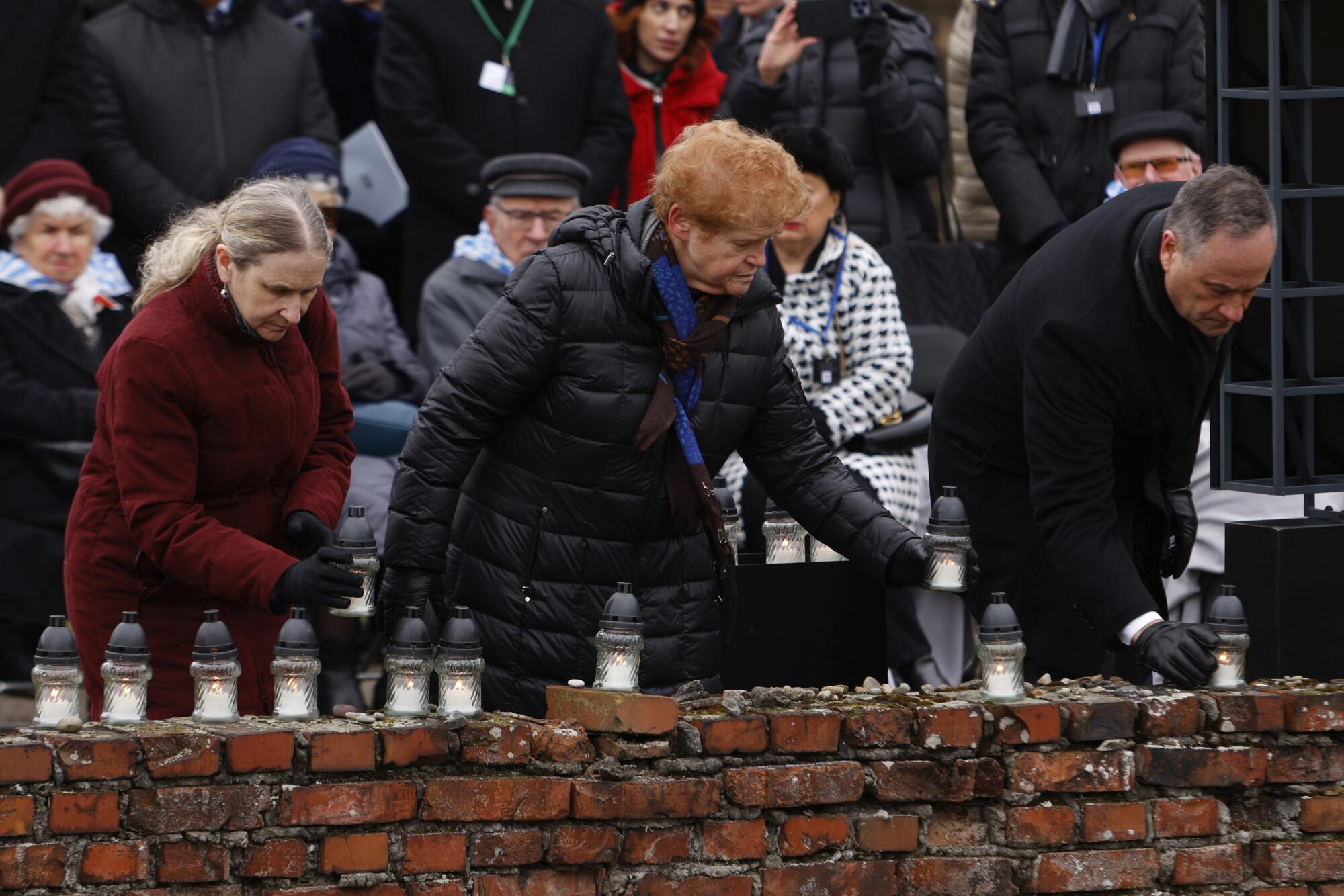 U.S. Second Gentleman Doug Emhoff, right, and Deborah Lipstadt, center, place candles along a brick wall.