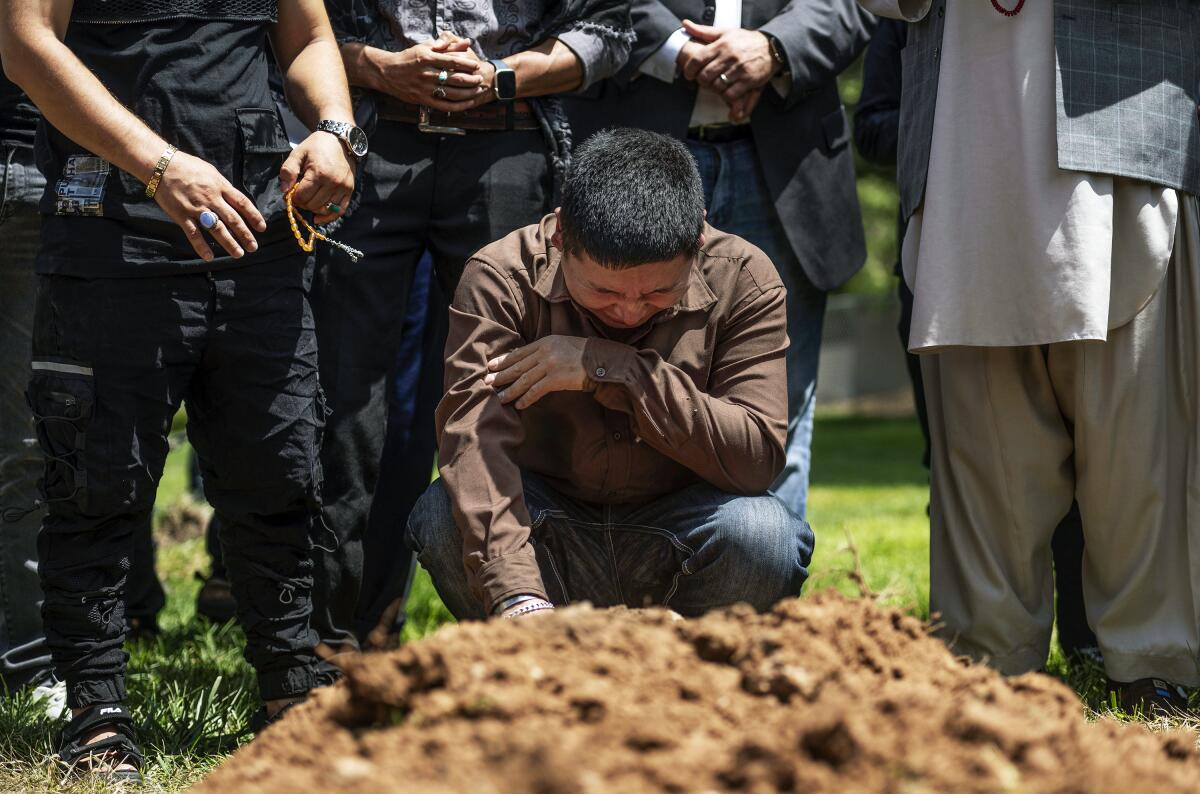 A man in a brown long-sleeved shirt and jeans cries over a mound of fresh dirt on the ground 