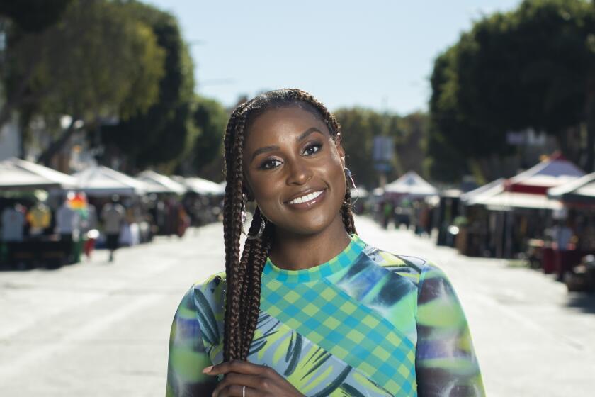 Issa Rael holds her long braided hair in the middle of a street while wearing a bright green patterned outfit