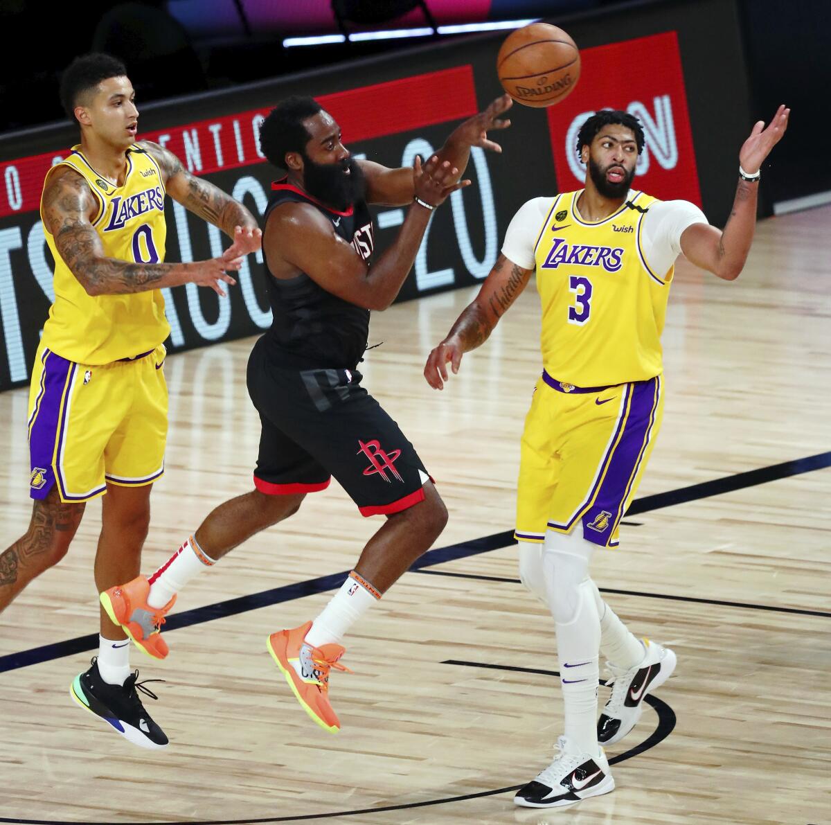 Rockets guard James Harden, center, passes the ball while defended by Lakers forwards Kyle Kuzma, left, and Anthony Davis.