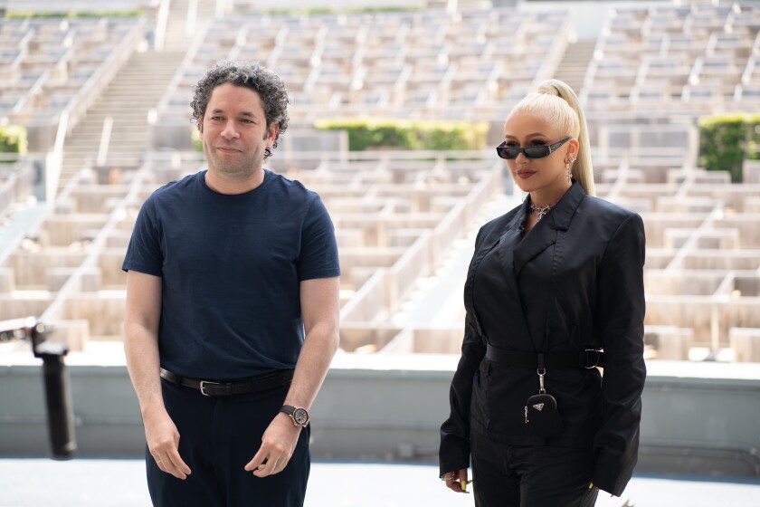 A man, left, and a woman in sunglasses stand in the foreground, with empty arena seats in the background