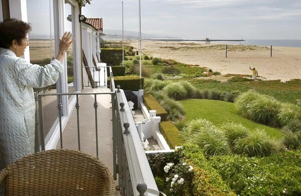 A resident waves to a neighbor from the balcony of her beachfront home on Balboa Peninsula in Newport Beach. Recently, the California Coastal Commission sent letters to homeowners along East Oceanfront, saying that the lawns, shrubbery and flowers they installed are "unpermitted landscaping on public beach."