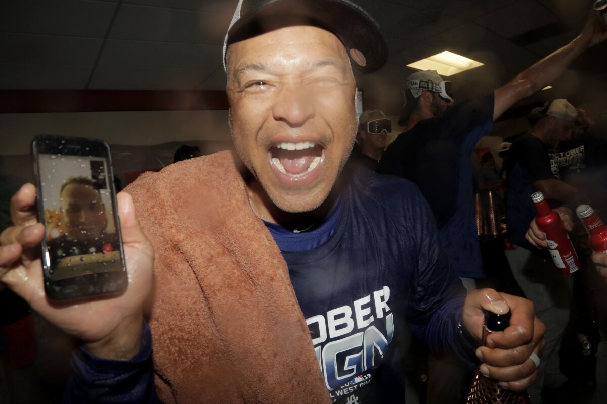 Dodgers manager Dave Roberts holds a cell phone during a video conference with injured infielder Max Muncy as the team celebrates its seventh straight National League West . (AP Photo/Julio Cortez)