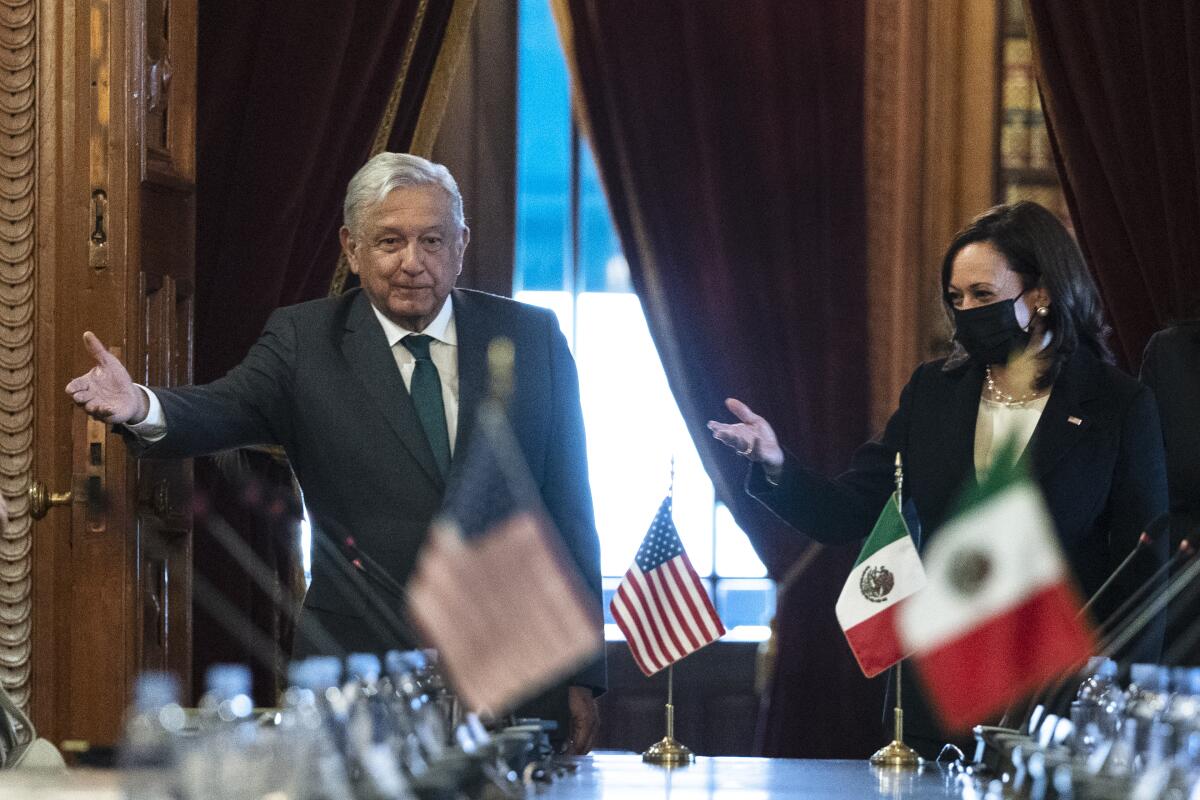 Mexico's president stands with Vice President Kamala Harris before a table with small U.S. and Mexican flags. 