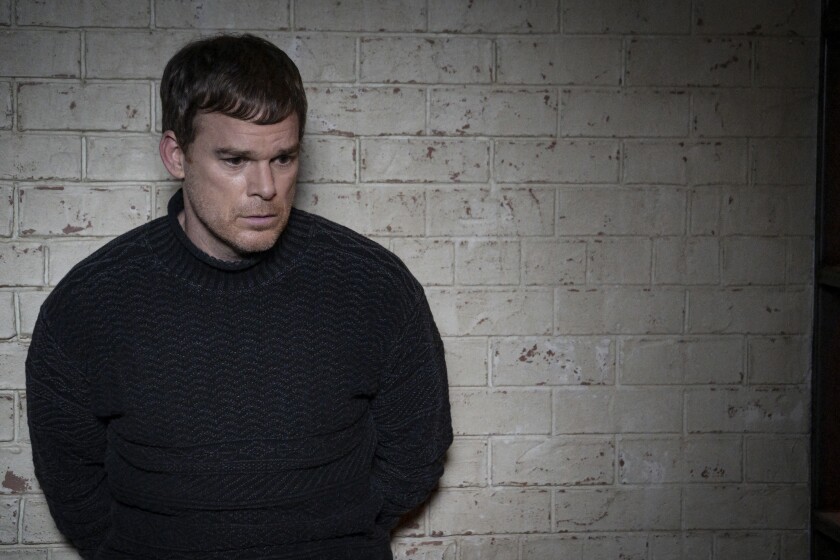 A man in a sweater leaning against a white brick wall in a dim room