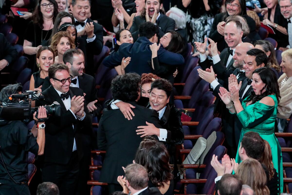 Actor Song Kang Ho hugs director Bong Joon Ho while an audience gives a standing ovation
