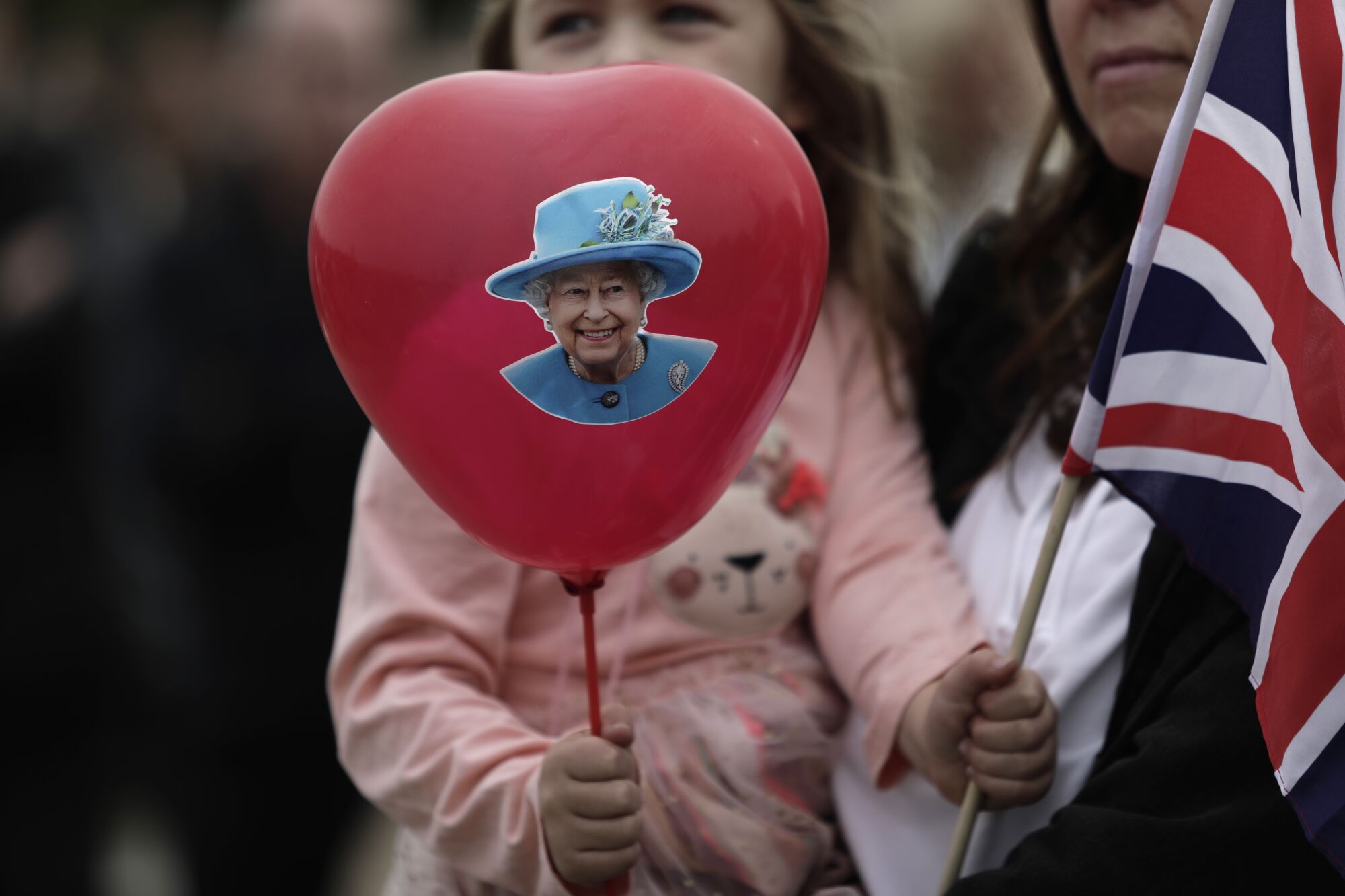 A girl holds a balloon with the Queen's picture and a Union Jack flag.