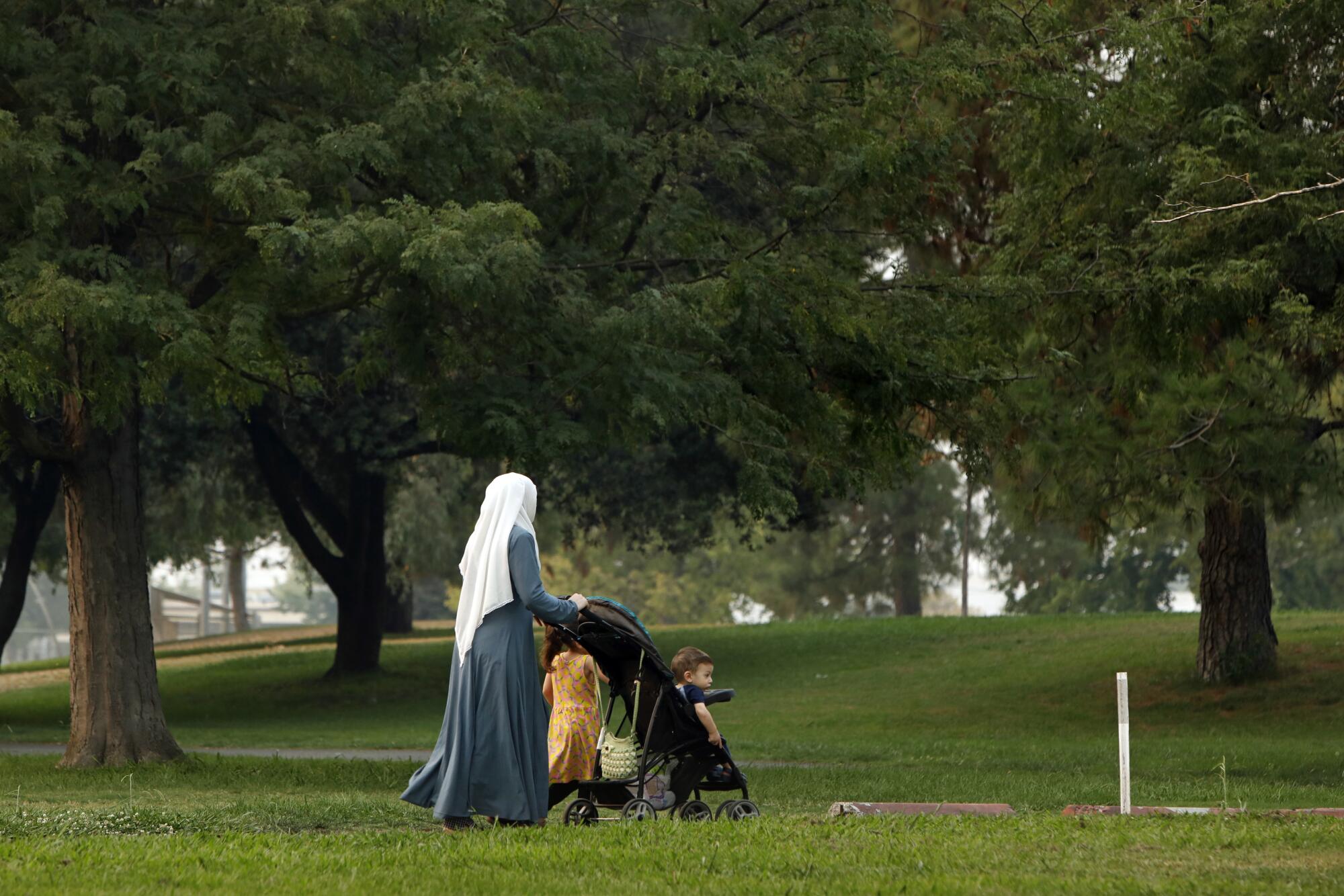 A woman pushes a child in a stroller while another walks beside them in a park