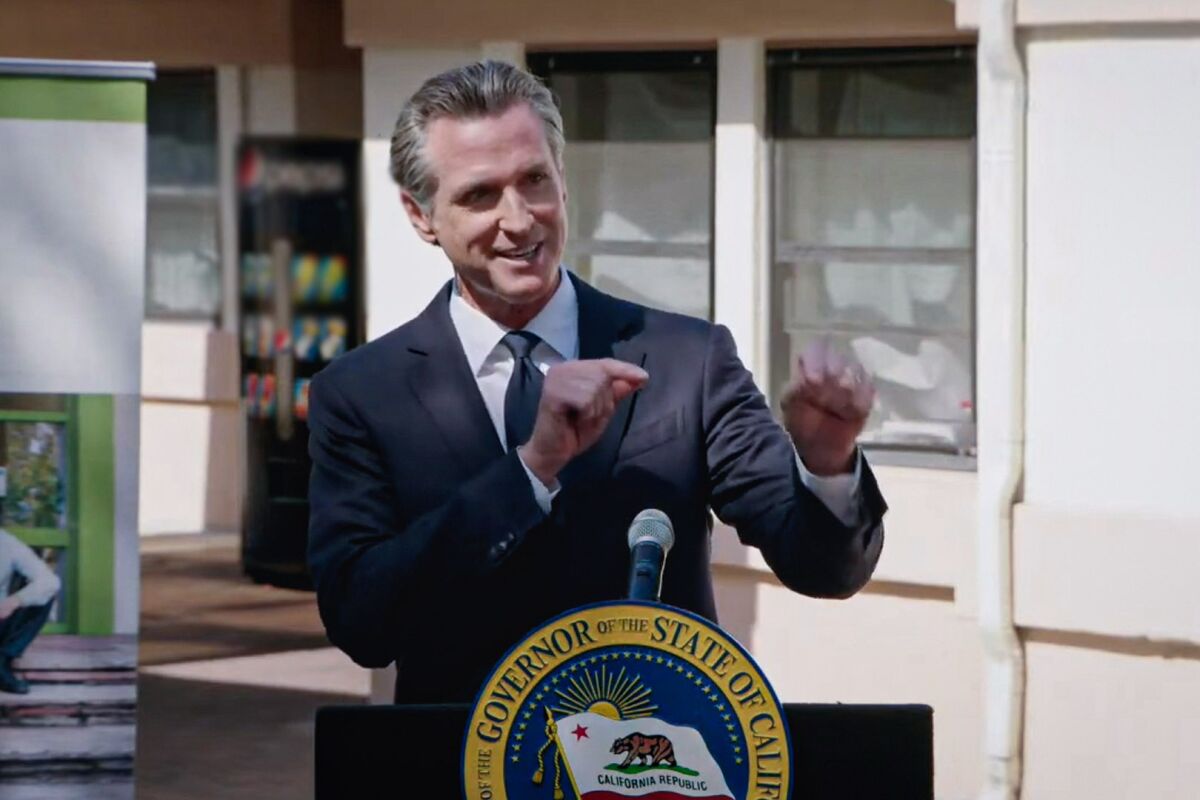Gov. Gavin Newsom smiles and stands behind a podium. 