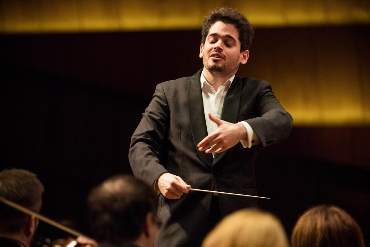 A man holds a baton in one hand as he conducts an orchestra
