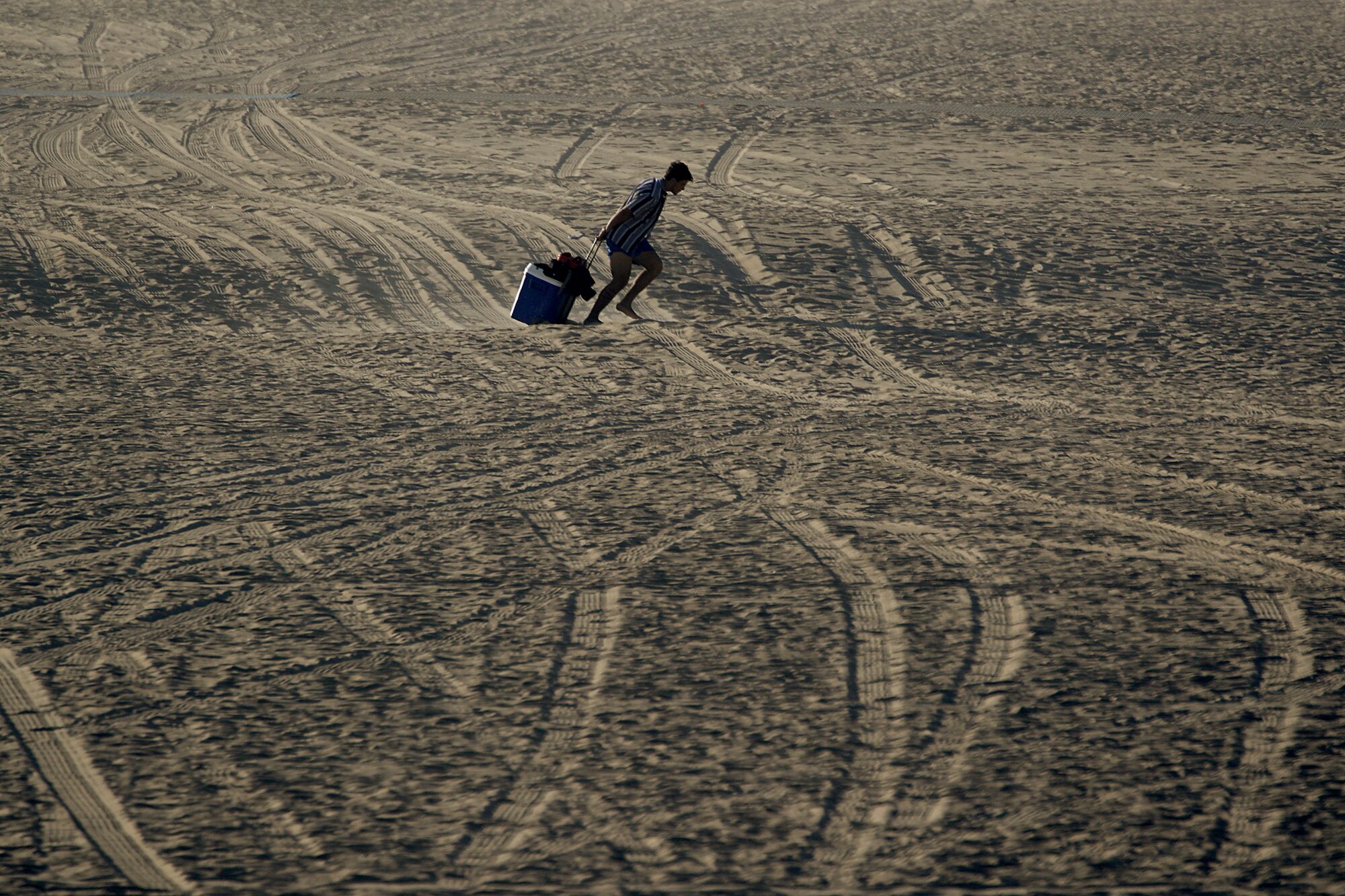 A beachgoer drags a cooler across the sand at Huntington Beach on Monday.
