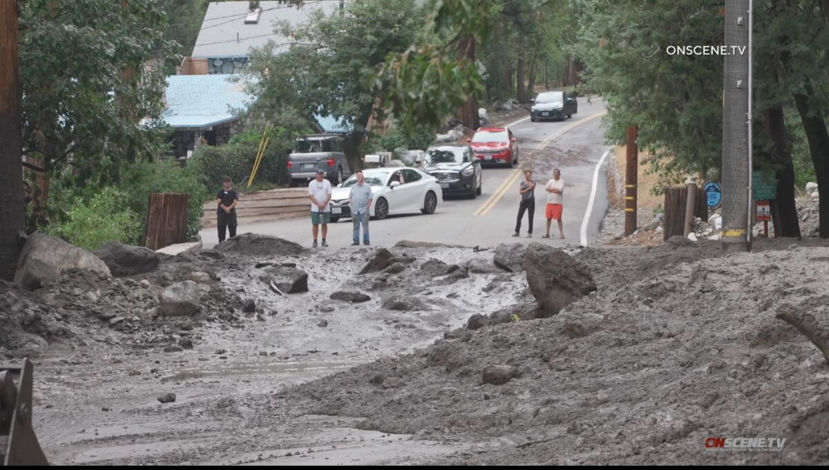 A road is blocked by several feet of mud as residents look on from a nearby street.