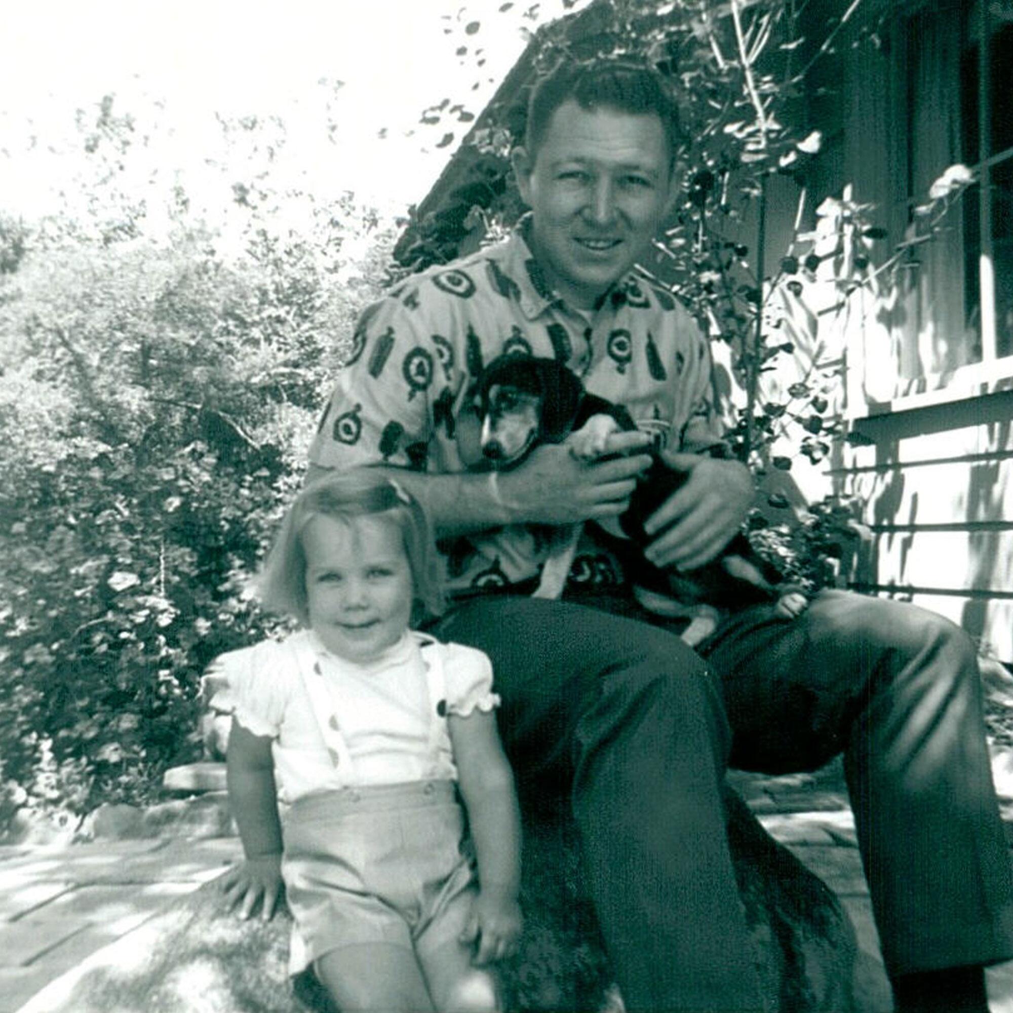 A family photo of a man with his young daughter and a small dog on his lap