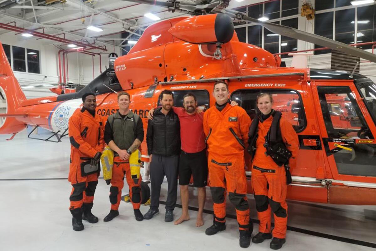 Six people pose in front of a Coast Guard helicopter.