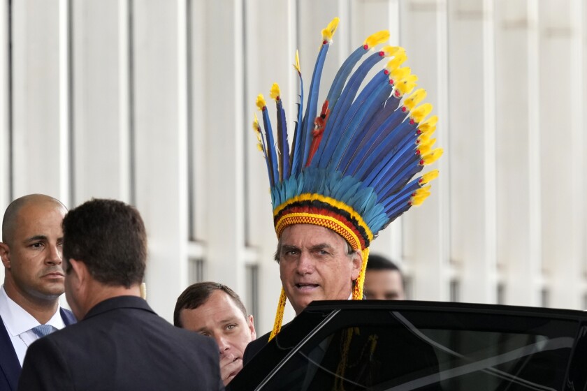 FILE - Brazil's President Jair Bolsonaro, wearing a traditional Paresi Indigenous headdress, leaves after participating in a ceremony where he was decorated with the Medal of Indigenous merit, at the Ministry of Justice, in Brasilia, Brazil, March 18, 2022. The accolade scandalized environmentalists, human rights activists and Indigenous groups who see the president’s push for development within Indigenous territories as profoundly damaging. (AP Photo/Eraldo Peres, File)