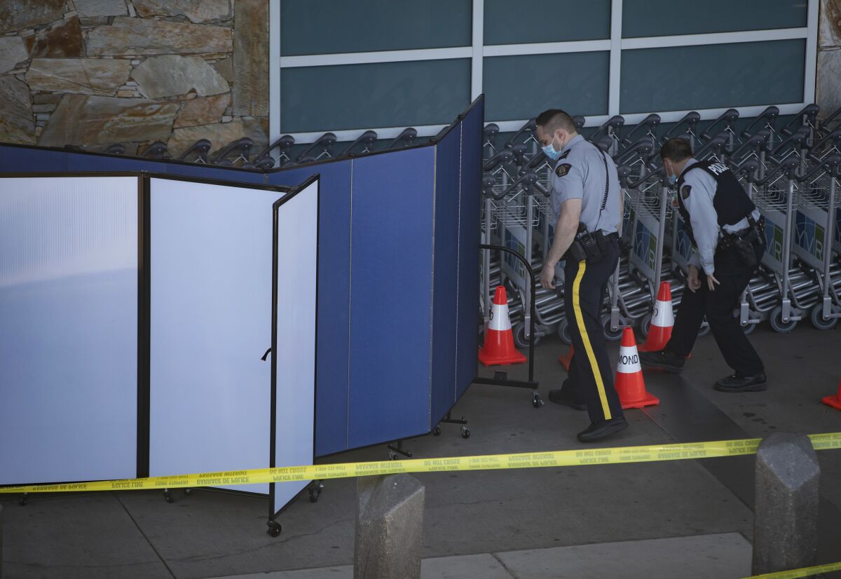 Royal Canadian Mounted Police officers search around rows of luggage carts as screens block off an area of the sidewalk after a shooting outside the international departures terminal at Vancouver International Airport, in Richmond, British Columbia, Sunday, May 9, 2021. (Darryl Dyck/The Canadian Press via AP)
